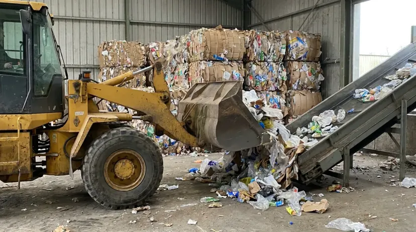 Pá-carregadeira alimenta prensa em central de triagem — meta de reciclagem 2026